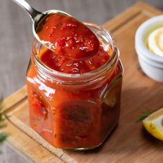 a spoon full of sauce sitting on top of a wooden cutting board next to lemon slices