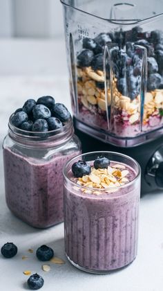 two glasses filled with blueberry smoothie next to a blender full of fruit