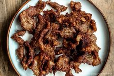 a white plate topped with fried meat on top of a wooden table next to a knife and fork