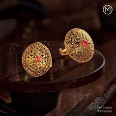 two gold cufflinks with red stones sitting on top of a wooden table