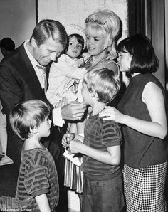 an old black and white photo of a man holding a baby surrounded by other people