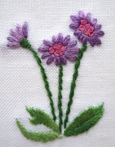 three purple flowers with green stems on a white cloth embroidered onto the side of a piece of fabric