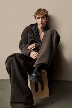 a young man sitting on top of a wooden block with his foot propped up against the wall