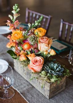 a wooden box filled with flowers on top of a table next to plates and wine glasses