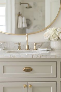 a bathroom vanity with marble counter top and gold faucet, round mirror above it