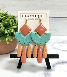 the clay and wood earrings are hanging on a stand next to a potted plant