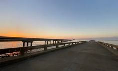 the sun is setting on an empty road by the water