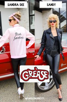 two women in black leather outfits standing next to a red car with the words grease on it