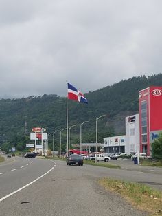 cars are driving down the road in front of a gas station and flagpoles