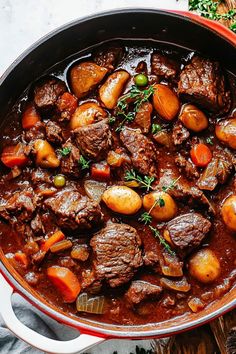 beef stew with carrots, potatoes and peas in a red pot