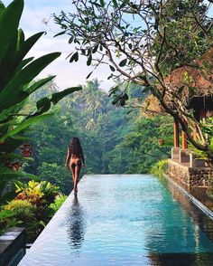 a woman is walking along the edge of a swimming pool with trees in the background