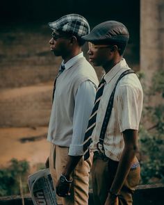 two men standing next to each other wearing ties and hats with newspaper in front of them