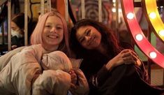 two women sitting next to each other in front of a neon light display at an amusement park