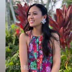 a woman with long black hair wearing a colorful dress and flower earrings smiling at the camera