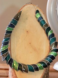 a necklace made out of green and blue beads sitting on top of a piece of wood