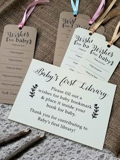 three baby's first library tags with ribbons on top of a table next to crocheted cloth