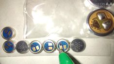 a pair of green scissors is next to some buttons on a white surface with blue and yellow letters