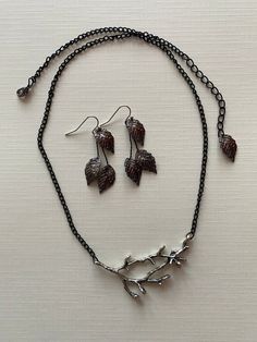 a necklace and earring set made out of metal with leaves on chain hanging from it