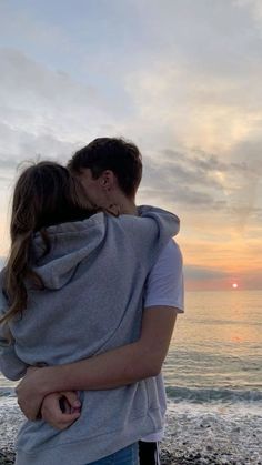 a man and woman hugging on the beach at sunset