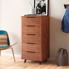 a wooden chest of drawers next to a blue chair in a room with white walls