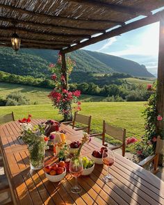 a wooden table topped with bowls of fruit on top of a lush green hillside covered in flowers