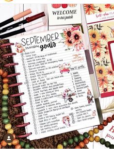 an open planner with flowers on it next to some beads and other items that include pens