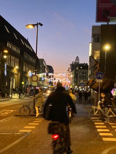 a man riding a bike down a street next to tall buildings and traffic lights at night