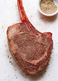 a piece of raw meat sitting on top of a white counter next to a small bowl of seasoning