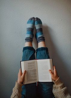 a person is laying down with their legs crossed and holding an open book in front of them