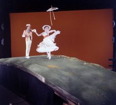 two people dressed in white are dancing on a stage with an umbrella over their heads