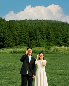 a man and woman standing in the grass looking through binoculars