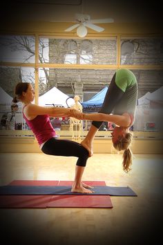 two women doing yoga poses in front of a window