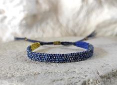 Narrow hand loomed fiber bracelet in indigo blue shades with golden sparkle.   Woven with silk, cotton and metallic thread. The warp yarn is durable linen in navy blue. Tiny brass beads at the ends of the ties. This is a slim but sturdy weaving that reminds of Lapis Lazuli - different beautiful blue shades with shimmering spots of gold. Simple, textile, minimalist. Width: 7 mm / 0.27'' Woven length: 13 cm / 5.1'' Wrist size easily adjustable with a macrame slipknot closure. Carefully woven and w Blue Woven Friendship Bracelets For Festivals, Blue Woven Bracelets As A Gift, Blue Woven Bracelets As Gifts, Blue Woven Bracelet Perfect For Gifting, Blue Woven Bracelet Perfect For Gift, Blue Woven Braided Bracelets For Festival, Blue Woven Braided Bracelet For Festivals, Handwoven Blue Bracelet Gift, Golden Sparkle