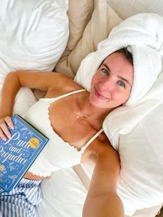 a woman laying in bed with a book on her chest and towel over her head