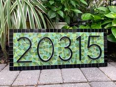 a green mosaic tile sign with the number 2055 on it's side in front of some plants