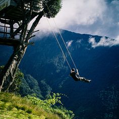 a man is swinging from a rope in the air on a mountain side with trees