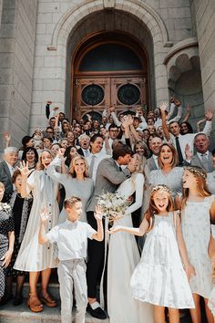 a large group of people standing in front of a building with their hands up and smiling