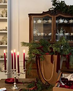 a table with candles and christmas decorations on it in front of a china hutch