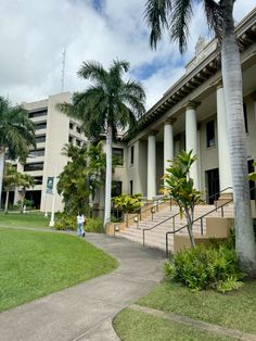 the building has columns and palm trees in front of it, along with a walkway