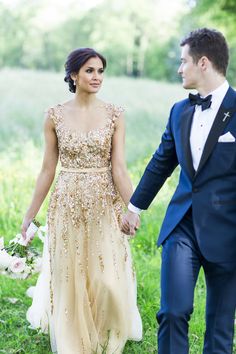 a bride and groom holding hands walking through the grass