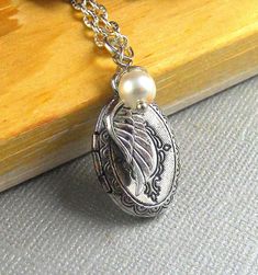 "This Vintage inspired necklace is 28\" long. Small oval silver finished locket with Victorian patterns engraved on the sides is decorated with antique finished tiny silver wing and white swarovski pearl. Pendant locket is finished with silver chain and silver lobster clasp. Locket is almost 23mm in size and opens side ways. It has room for two photos! Thanks for looking:) ~Mani" Antique Silver Locket Necklace With Oval Pendant, Antique Silver Oval Pendant Locket Necklace, Silver Vintage Charm Oval Pendant Jewelry, Antique Silver Oval Pendant Necklace With Locket, Antique Silver Necklace With Oval Locket Pendant, Silver Oval Pendant With Vintage Charm, Antique Silver Oval Locket Necklace, Silver Necklaces With Oval Pendant Vintage Charm, Silver Necklace With Oval Pendant And Vintage Charm