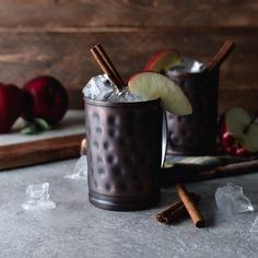 two glasses filled with apple cider next to cinnamon sticks and apples on a cutting board