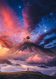 a man standing on top of a hill under a colorful sky filled with stars and clouds