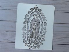 a paper cut image of the virgin mary with roses on it's side, in front of a wooden background