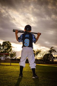 a young boy holding a baseball bat on top of his shoulder while standing in the grass