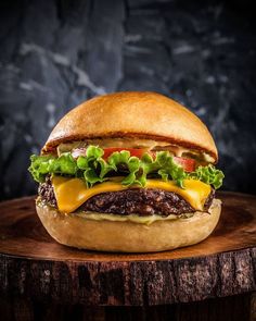 a cheeseburger with lettuce, tomato and other toppings on a wooden board