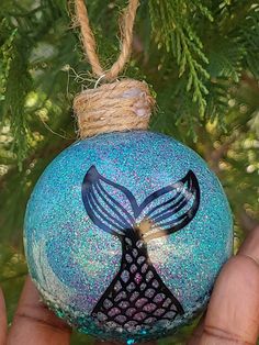 a hand holding a blue ornament with a mermaid tail on it