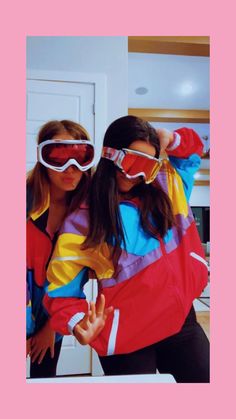 two girls wearing ski goggles and jackets in the mirror with their arms around each other