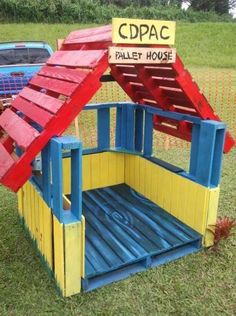 a small house made out of pallet wood and painted red, yellow and blue