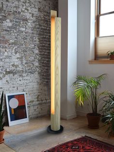 a floor lamp sitting on top of a rug next to a potted plant in front of a brick wall